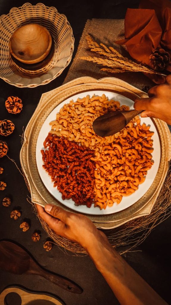 pexels-photo-12594696 Top view of a rustic macaroni dish with hands preparing using a wooden spoon.