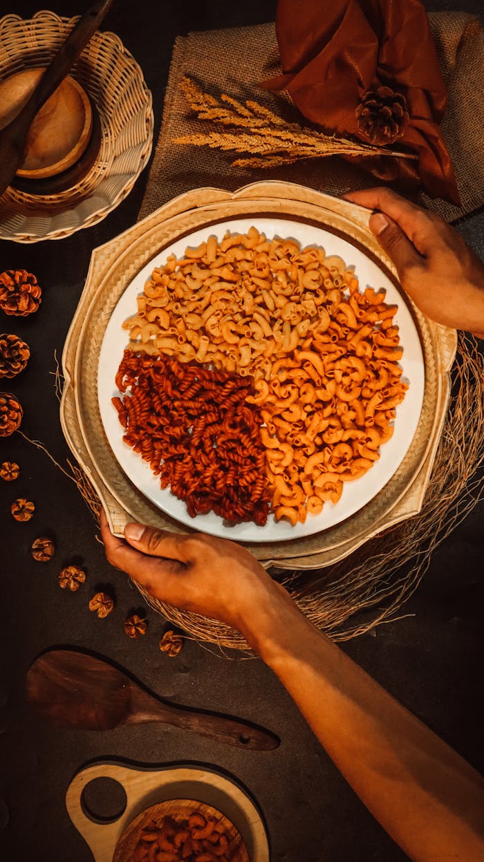about-img Close-up of mixed colored pasta served in a rustic setting with hands holding the plate.
