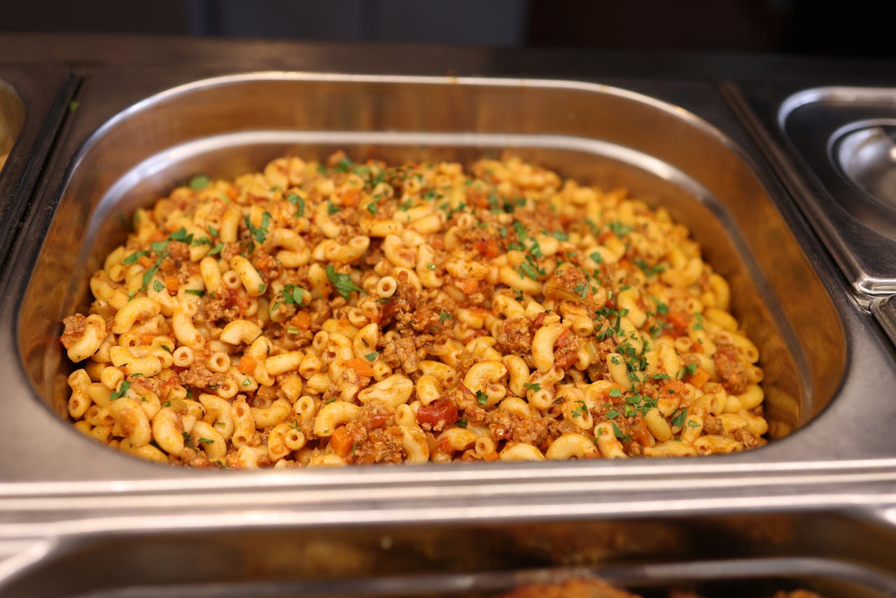 services-02 Close-up of a hot serving tray filled with macaroni and ground beef garnished with herbs.