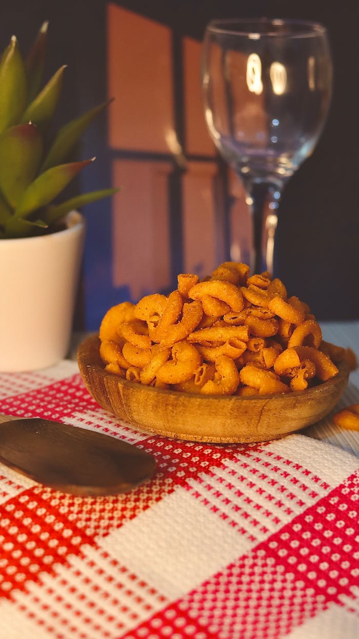 ours-journey Appetizing bowl of crunchy snacks on a checkered tablecloth with a wine glass in the background.