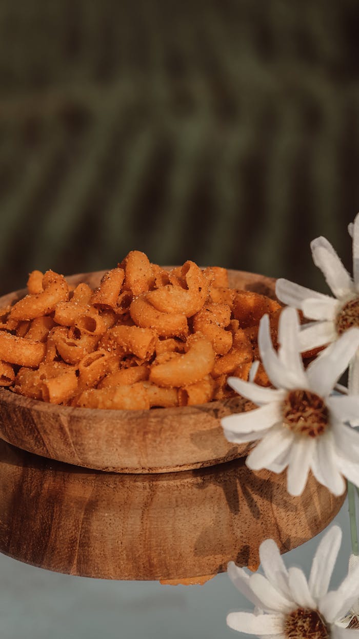 about-02 Close-up of a wooden bowl filled with spicy pasta surrounded by white daisies. Perfect for food photography.