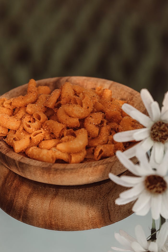 Delicious seasoned macaroni in a rustic wooden bowl, adorned with white flowers for a natural touch.